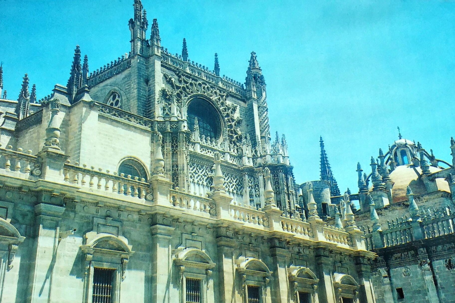 Exterior view of Catedral de Sevilla showing detailed Gothic stonework and spires under a clear blue sky.