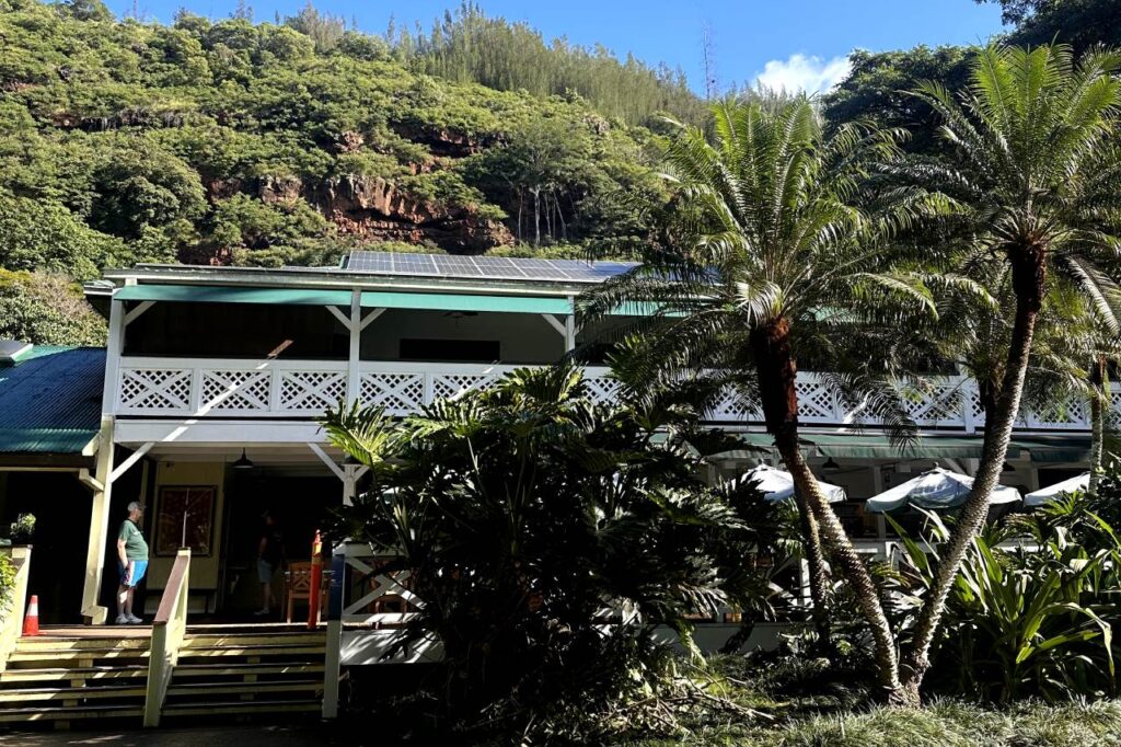 A large, two-story building with green under palm trees and tropical plants in Waimea Valley in Oahu, Hawaii.