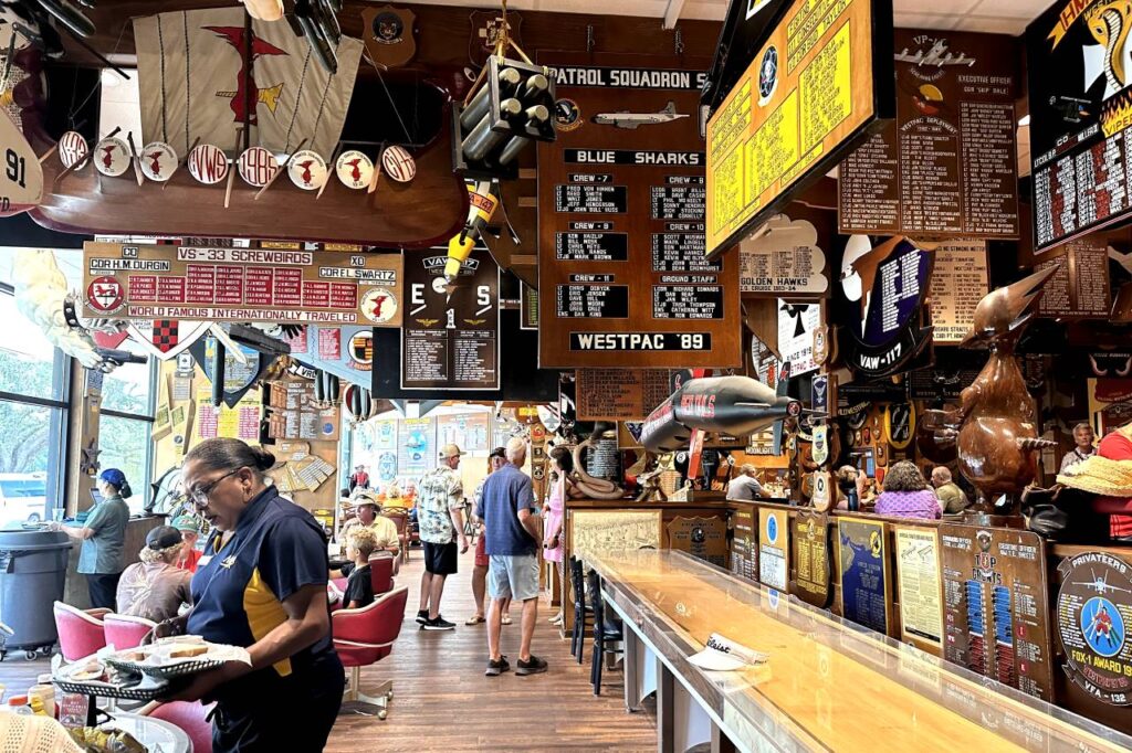 The interior of the Cubi Bar Café inside the National Naval Aviation Museum in Pensacola, filled with naval memorabilia and plaques hanging from the walls and ceiling.