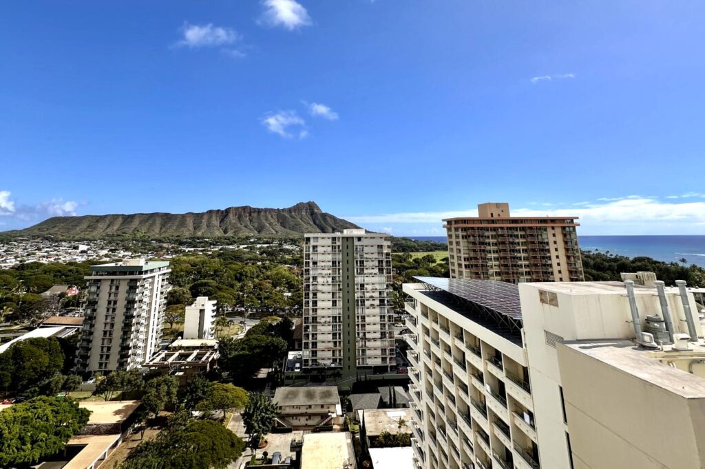 A view of Diamond Head Crater with tall buildings in the foreground and a clear blue sky above. Oahu, Hawaii. Mountain View room, from Hyatt Hotel.