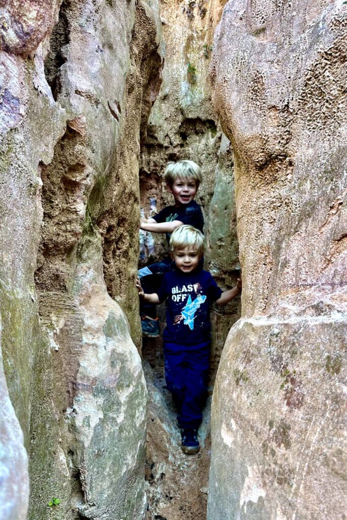 Two young children are happily exploring a narrow crevice between tall, weathered canyon walls at Providence Canyon in Georgia.