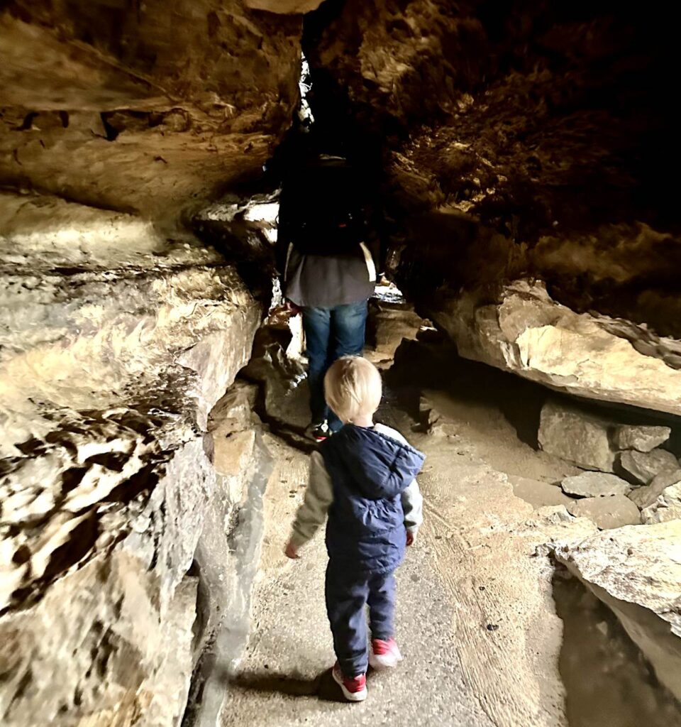 A child walking through a narrow cave passage with uneven rocky walls towering above them. Ruby Falls cave walk in Chattanooga, Tennessee