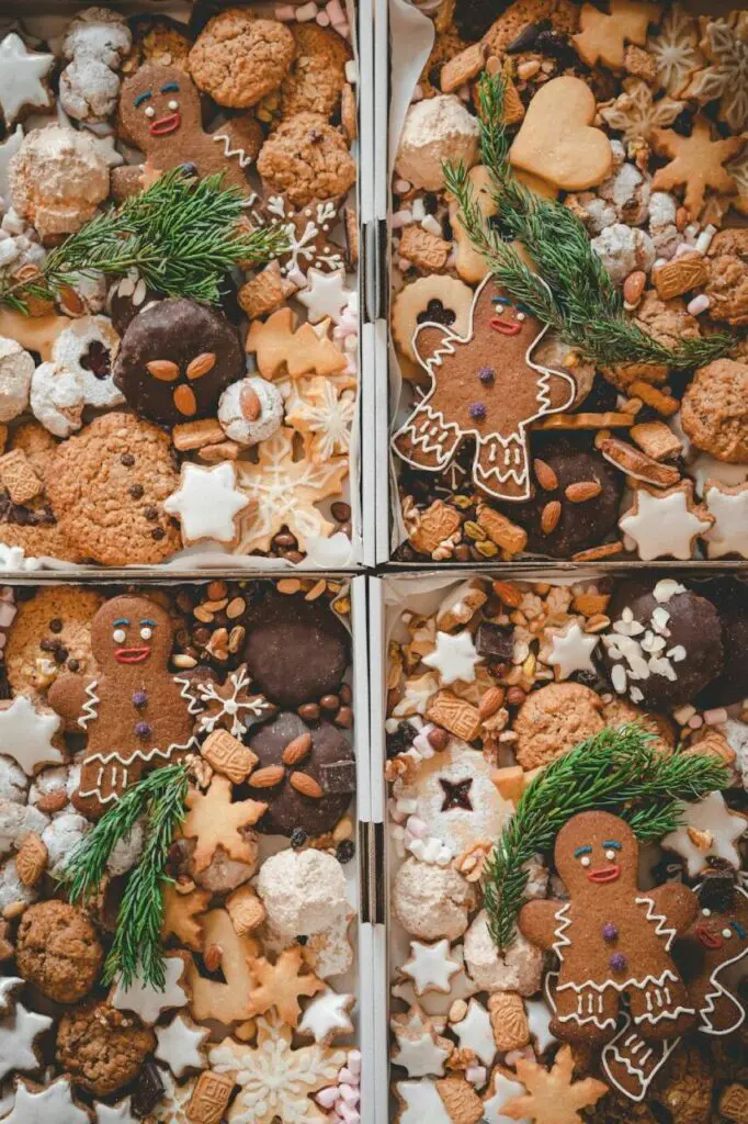 An assortment of holiday cookies and gingerbread decorated with icing, displayed with sprigs of pine at a Christmas market.