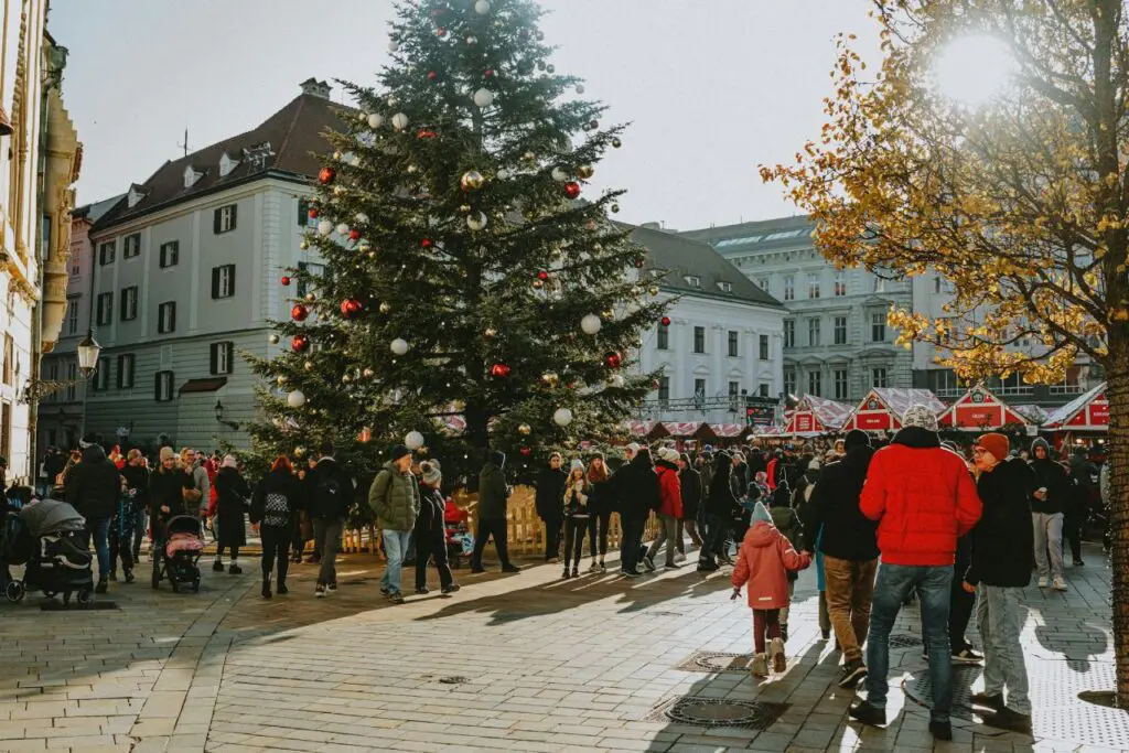 A decorated Christmas tree with red and white ornaments in the middle of a festive market surrounded by crowds enjoying the holiday atmosphere. Vienna.