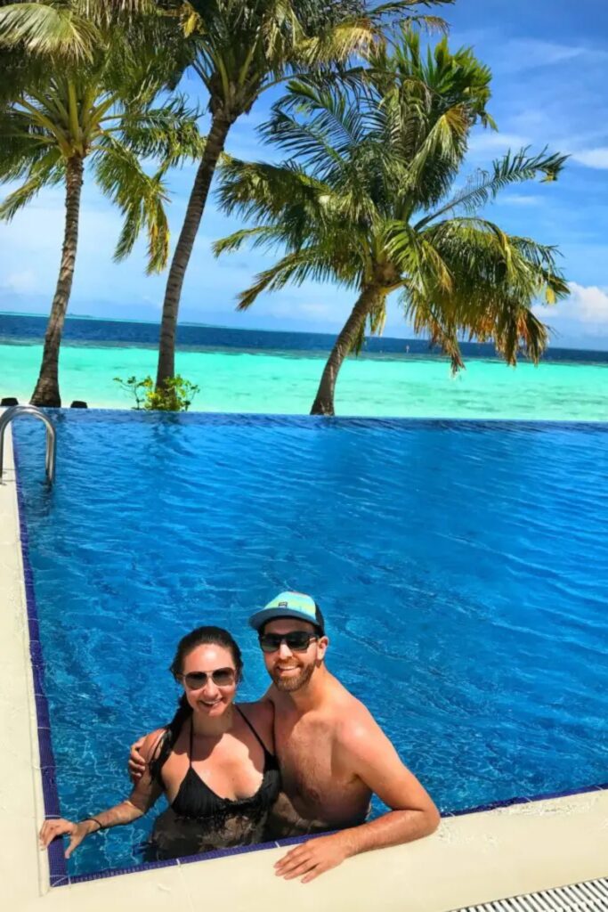 A couple smiles while embracing in an infinity pool, with tropical palm trees and the clear blue ocean in the background. Earn more travel rewards
