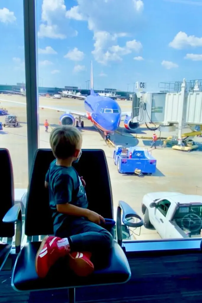 A young child sits in an airport lounge, looking out at a suthwest airplane parked at the gate on a sunny day. Southwest companion pass
