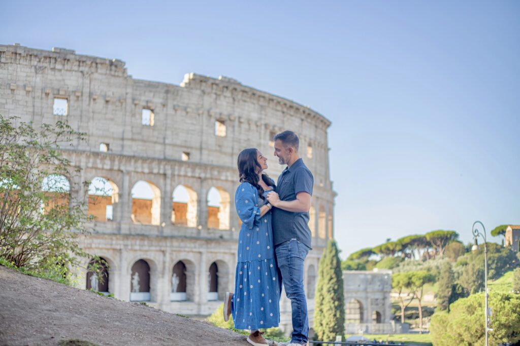 A couple smiles at each other standing in front of the Colosseum in Rome, Italy