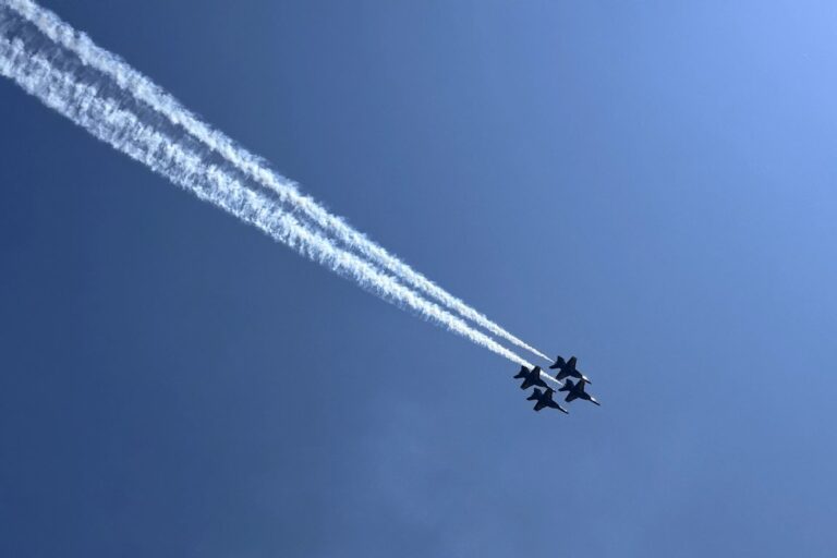 Four Blue Angels jets fly in tight formation with white smoke trails behind them against a clear blue sky. National Aviation Museum, Pensacola, Florida