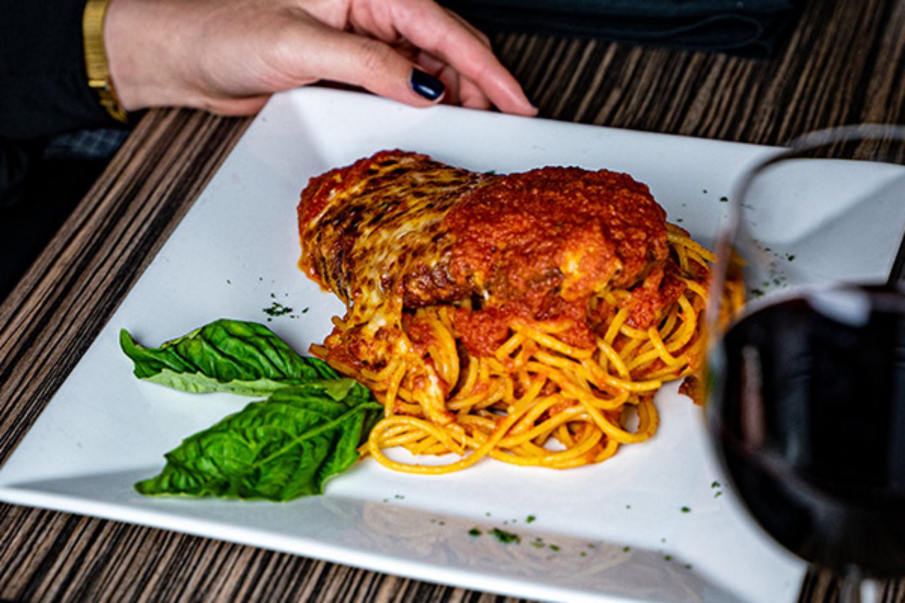 A close-up of a plate of chicken parmesan with melted cheese and marinara sauce, served over a bed of spaghetti. 