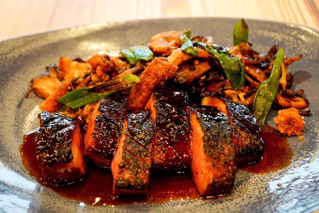 A seared duck breast with a caramelized, crispy skin, drizzled with a rich, dark sauce. The point