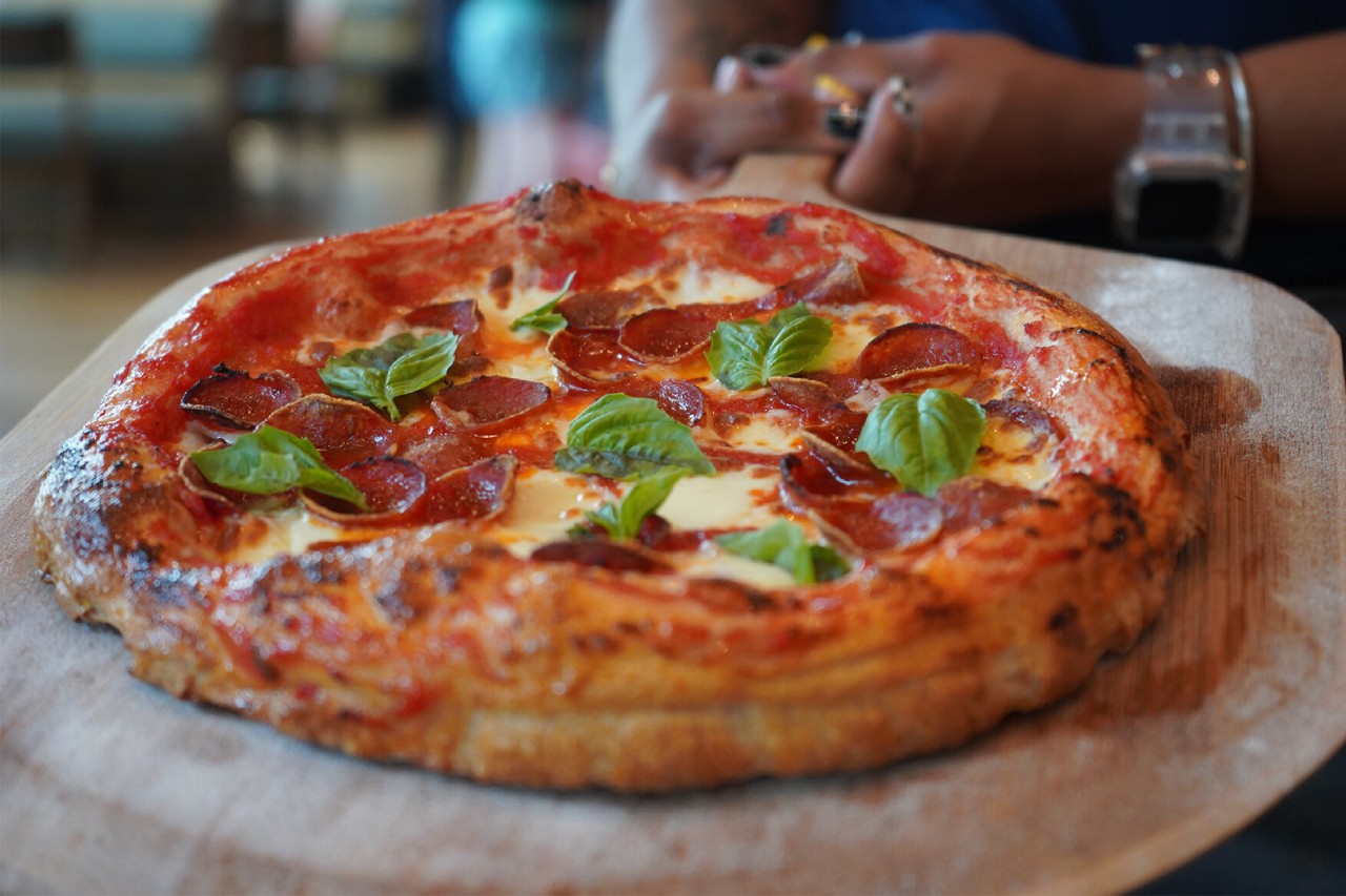 A freshly baked pepperoni pizza with a golden, slightly charred crust, topped with melted mozzarella, crispy pepperoni, and fresh basil leaves. The Point