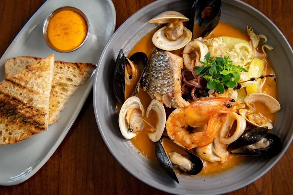 A bowl of seafood stew with mussels, clams, shrimp, squid, and a piece of white fish, all simmered in a rich, orange-colored broth. DC Restaurants for Families
