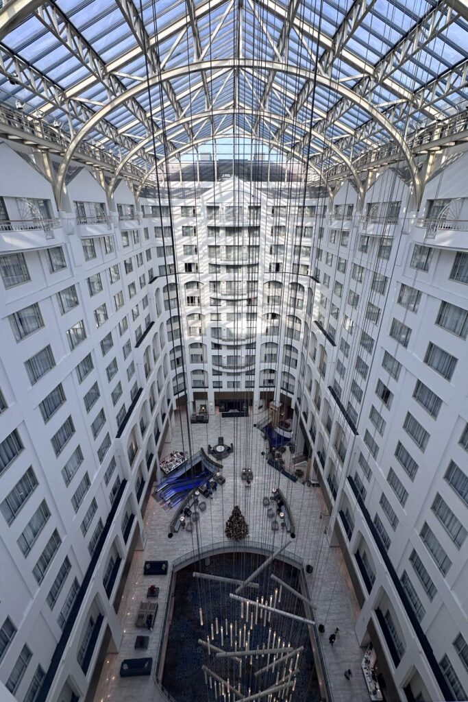 An upward view of a hotel atrium with a glass roof, featuring multiple floors and suspended lights. Grand Hyatt Washington DC. Washington DC Itinerary