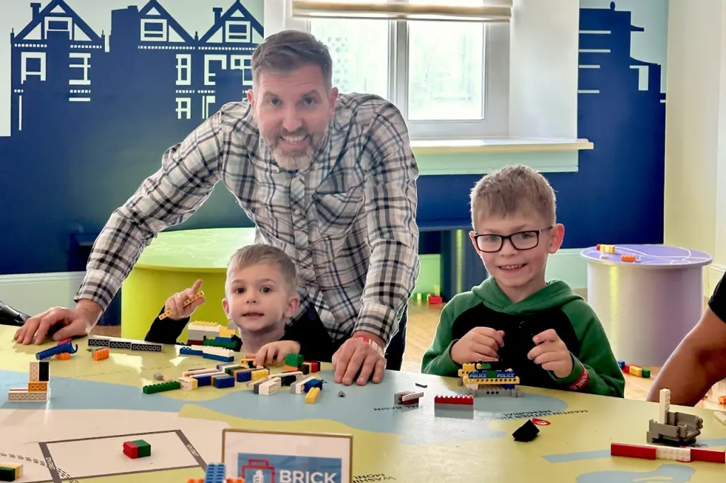 A father and two young boys building with Lego blocks at a hands-on exhibit table in the National Building Museum.