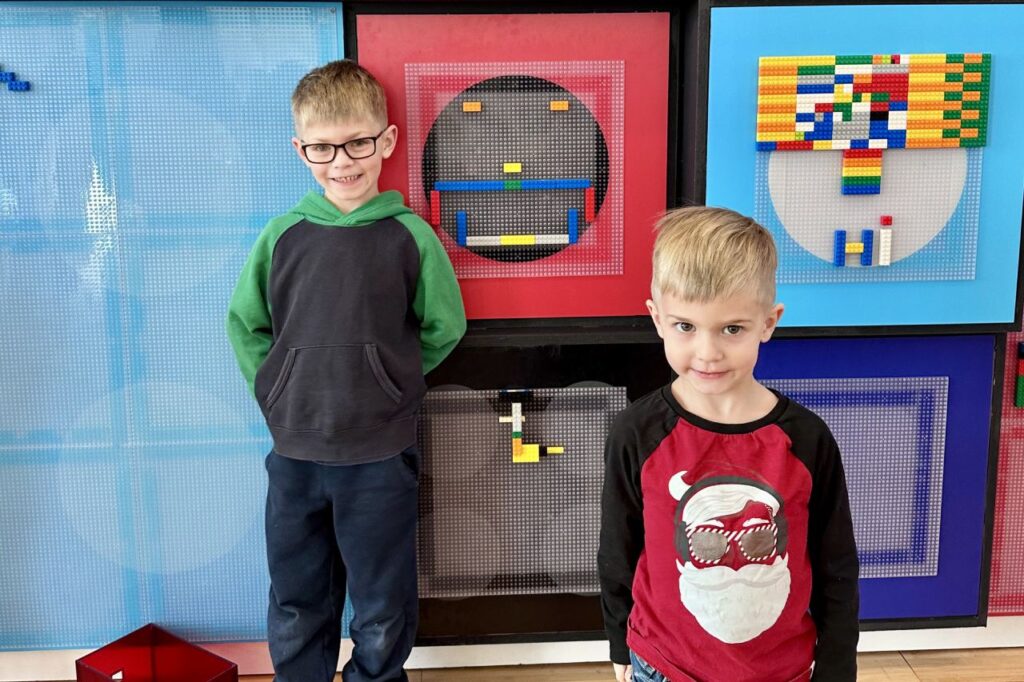 Two young boys posing in front of a Lego art display featuring colorful geometric designs. National Building Museum. Things to do in DC with Kids