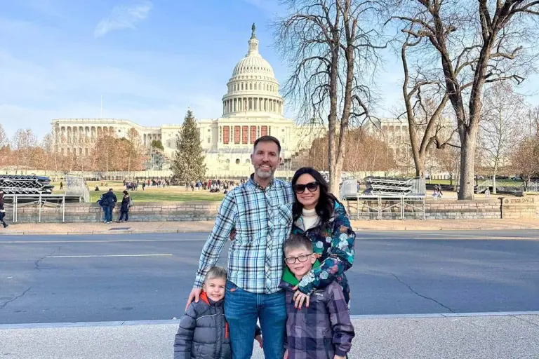 A family of four standing outside with the U.S. Capitol in the background on a sunny day. Washington DC Itinerary