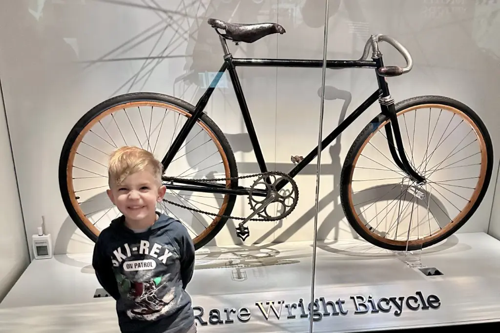 A young boy smiling in front of a vintage bicycle displayed at the Air and Space Museum exhibit. Free Things to Do in DC