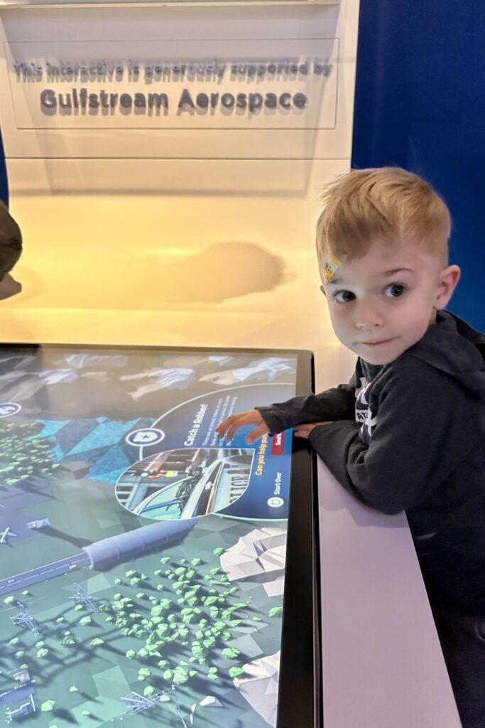 A young child interacting with a touch screen exhibit titled "Catch a Robber!" sponsored by Gulfstream Aerospace. Air and Space Museum. Free Things to Do in DC