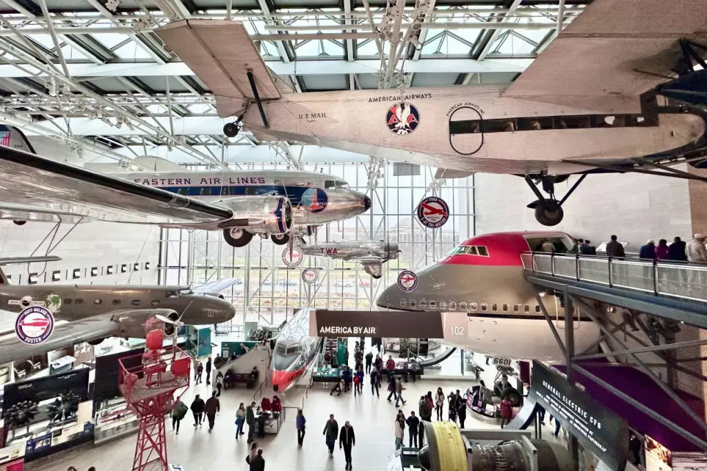 An indoor exhibit showcasing vintage airplanes from American and Eastern Airlines suspended in a museum, with visitors exploring the gallery below. Free Things to Do in DC