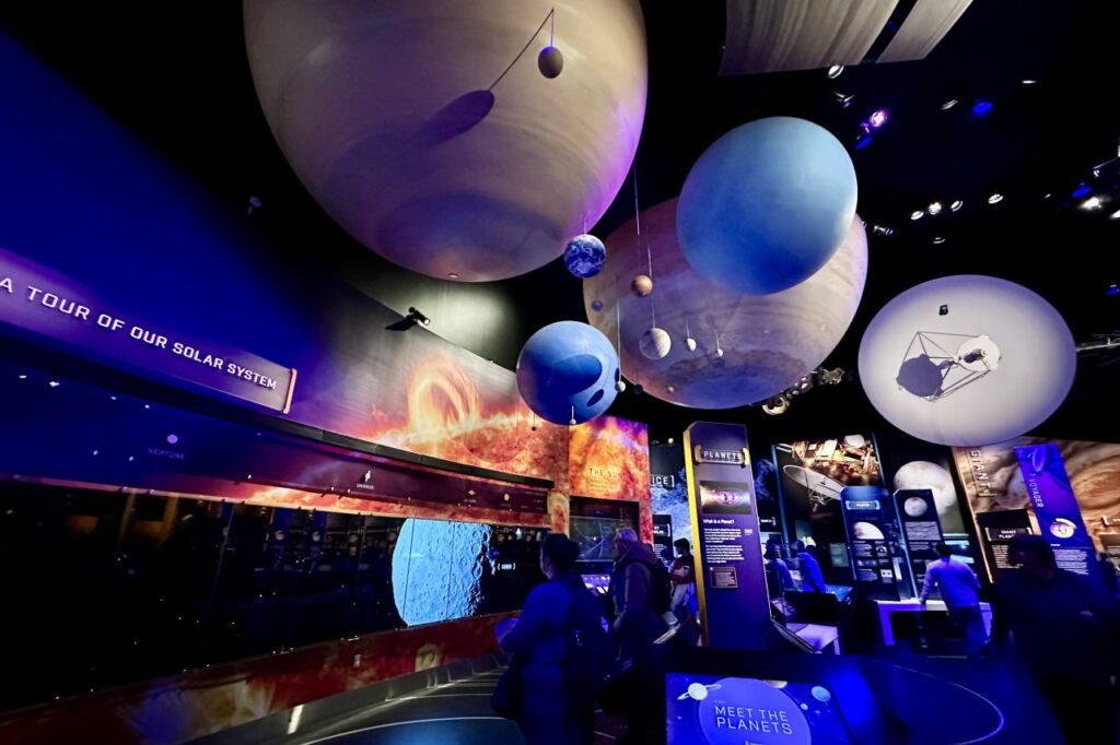 A planetary exhibit in a dark museum hall, with illuminated models of planets like Saturn, Jupiter, and Earth hanging from the ceiling. Air and Space Museum. Free Things to Do in DC