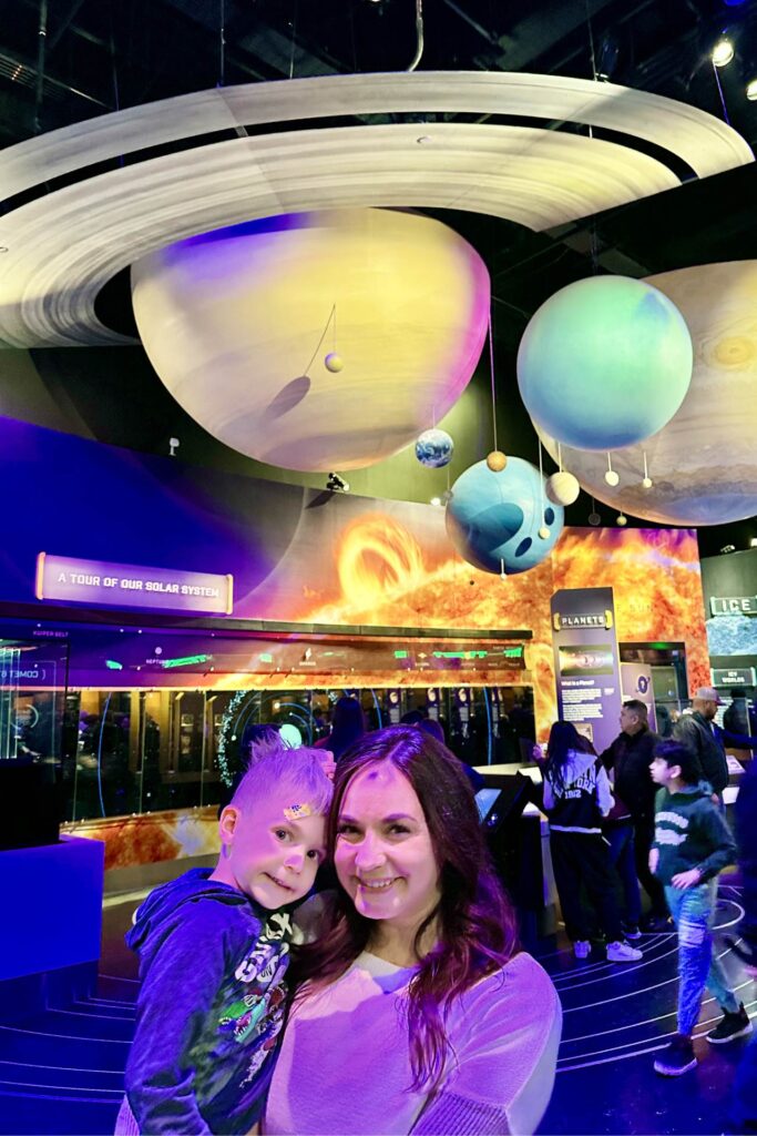 A woman holding a child in a museum exhibit featuring a model of the solar system with planets and a glowing representation of the Sun in the background. Air and Space Museum. Washington DC Itinerary