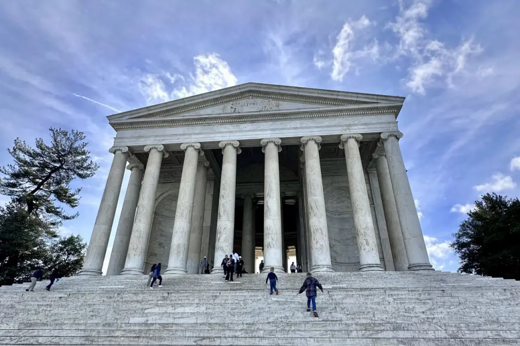 Jefferson Memorial seen from below the stairs, with the blue sky and clouds in the background.