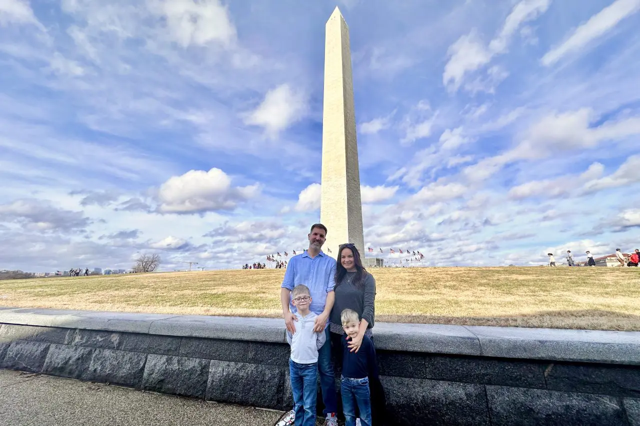 A family posing in front of the Washington Monument on a sunny day with a bright, partly cloudy sky.