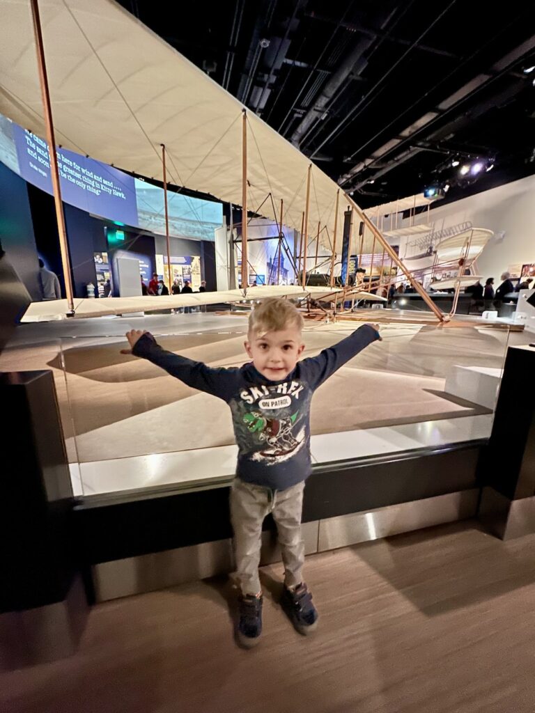 A bot stands in front of a model of the Wright plane, the first plane in flight, in the National Air and Space Museum in Washington, DC