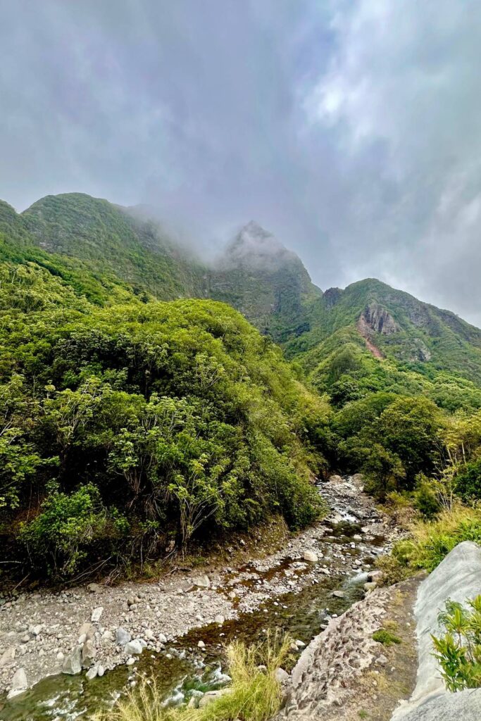 A misty view of green mountain peaks and a river winding through the valley floor in ʻĪao Valley.