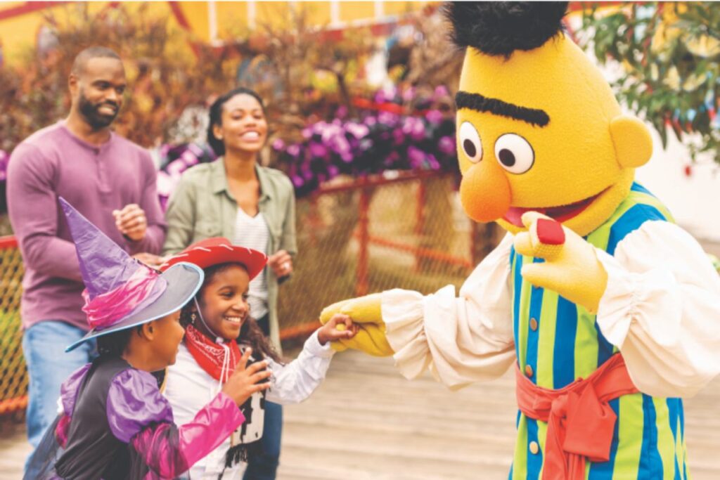 Children in costumes meet Bert from Sesame Street at Sesame Place while parents watch and smile during a family Halloween event.