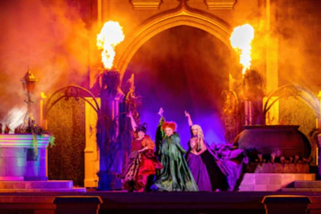 The Sanderson Sisters from Hocus Pocus performing on stage with cauldrons, fire effects, and colorful lighting during Disney’s Hocus Pocus Villain Spelltacular show.