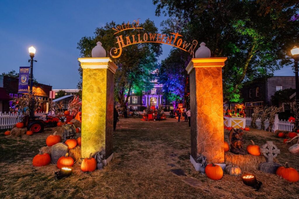 Entrance to the Spirit of Halloweentown festival in St. Helens, Oregon, with glowing pillars, pumpkins, hay bales, and colorful lights decorating the town square.