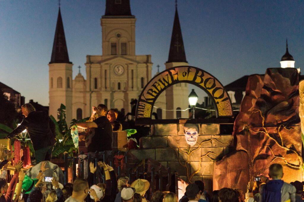 Krewe of Boo Halloween parade float in New Orleans with performers tossing beads to a crowd, with St. Louis Cathedral in the background.