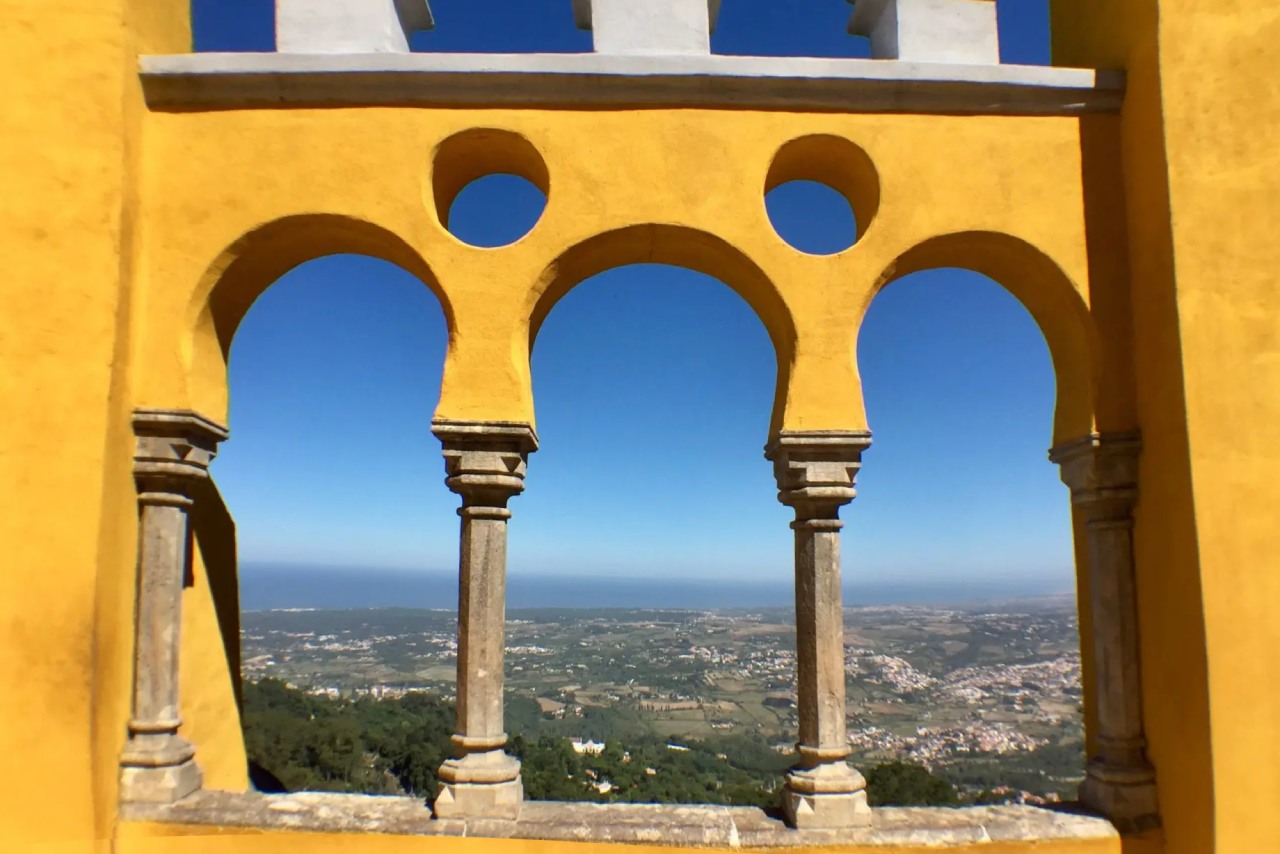 Yellow arched windows at Pena Palace in Sintra, Portugal, framing a sweeping view of the countryside and ocean beyond.