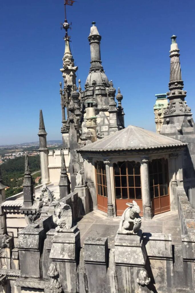 Gothic spires and stone sculptures on the rooftop of Quinta da Regaleira in Sintra, Portugal, with countryside views in the background. Visit Sintra