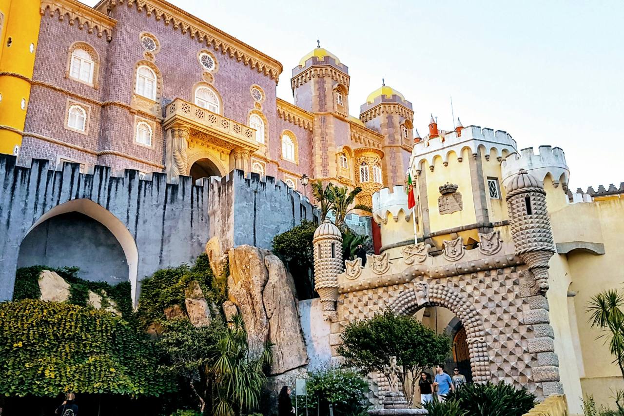 Entrance view of Pena Palace in Sintra, Portugal, showing the yellow and purple tiled facade with its ornate archway and fortress-like walls.