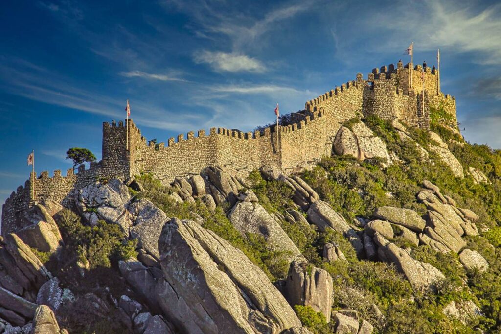 Castle of the Moors in Sintra, Portugal, with its medieval stone walls and towers stretching across the rocky hillside under a blue sky.