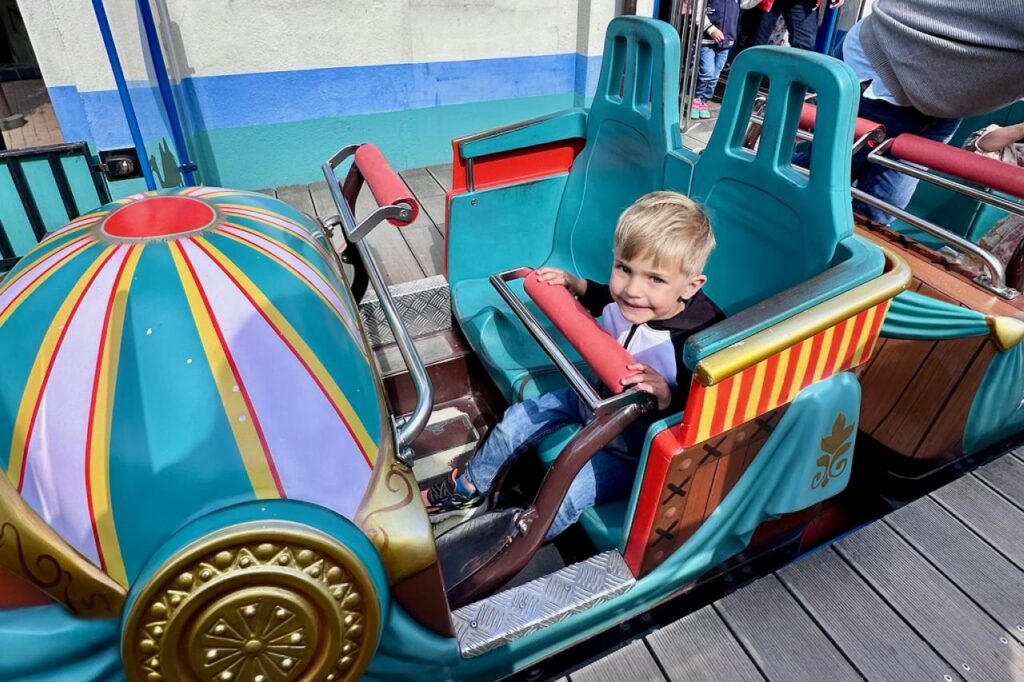 Small child seated in a colorful amusement park ride, smiling before it begins.