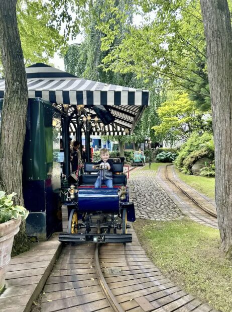 Child riding a small train through a wooded area inside Tivoli Gardens.