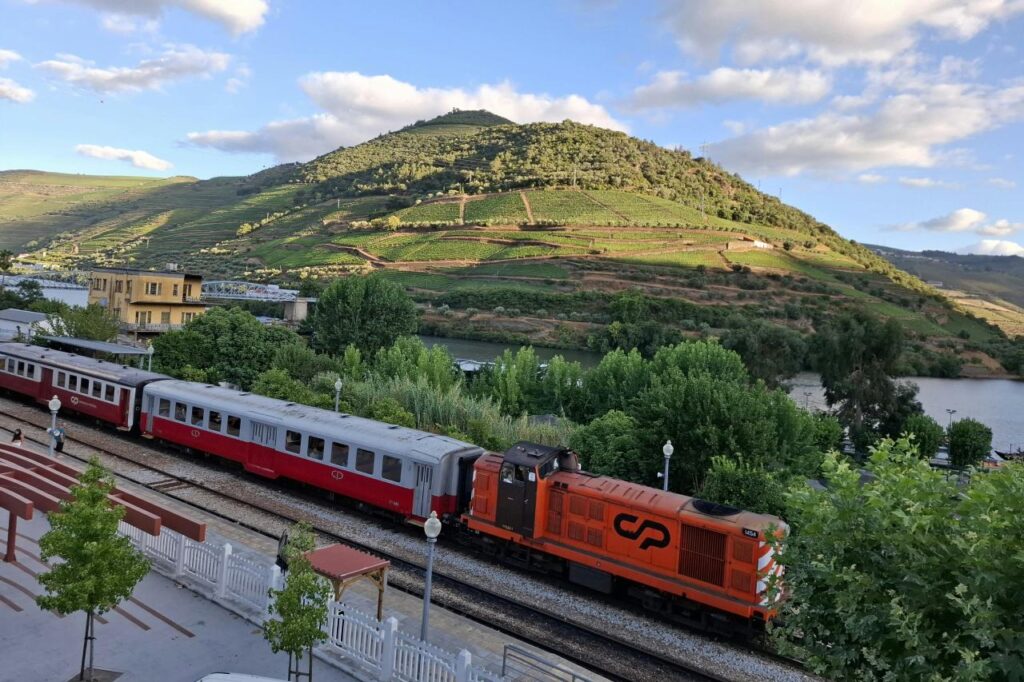 Historic CP train at Pinhão station in the Douro Valley, Portugal, with terraced vineyards covering the hillside behind it