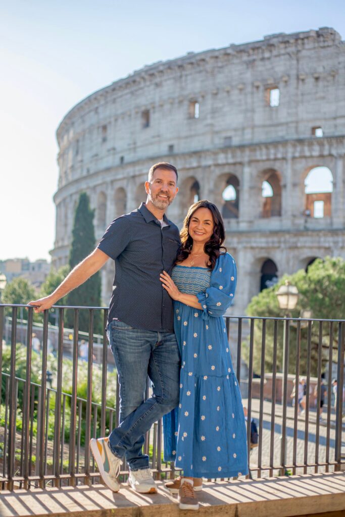 Couple posing together with the Colosseum in the background in Rome, standing by a railing in bright morning light.