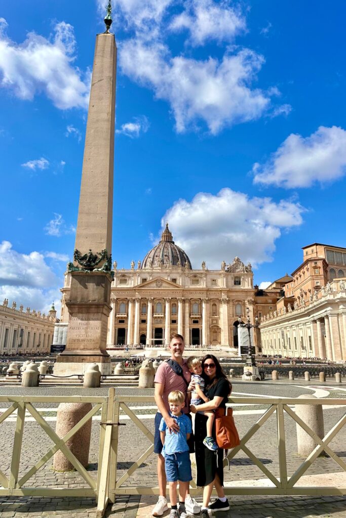 Family of four posing in St. Peter’s Square in Vatican City, with St. Peter’s Basilica and the tall obelisk behind them.