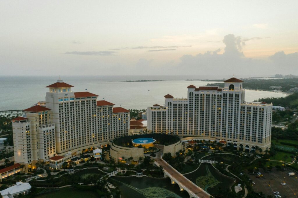 Aerial view of the Grand Hyatt Baha Mar resort at dusk, showing the two large cream-colored towers with red roofs, the pool area between them, landscaped groun…Aerial view of the Grand Hyatt Baha Mar resort at dusk, showing the two large cream-colored towers with red roofs, the pool area between them, landscaped grounds, and the calm blue waters of Nassau, Bahamas in the background