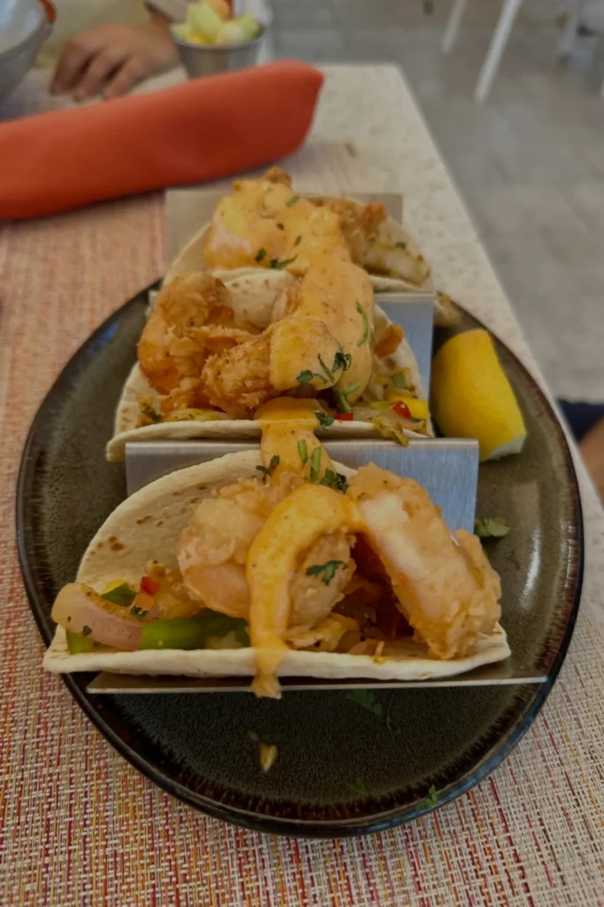 Three crispy fried fish tacos served on a dark plate with a wedge of lemon at a Baha Mar restaurant in Nassau, Bahamas.