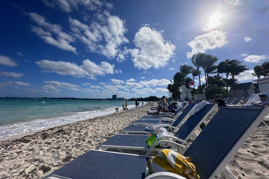 Cable Beach at Baha Mar on a sunny and breezy January day, with a row of navy blue loungers facing the turquoise water and palm trees swaying in the wind.