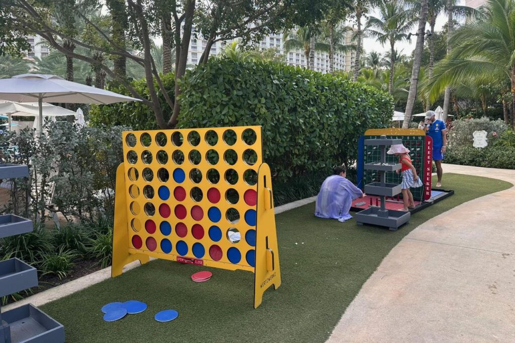Two kids playing oversized lawn games including giant Connect Four at Baha Mar, surrounded by palm trees and resort grounds.