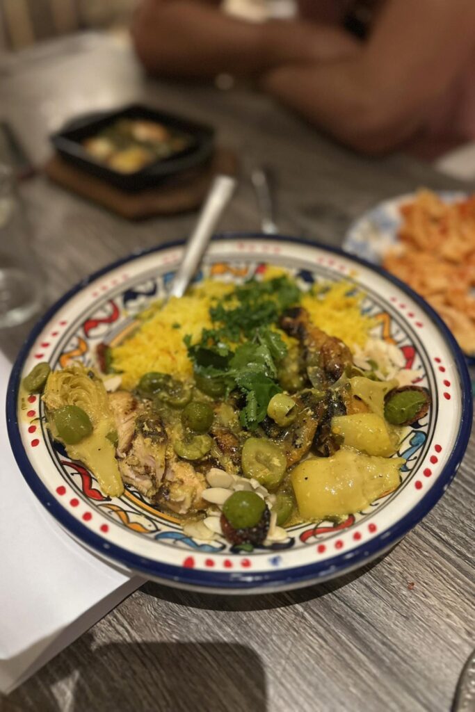 Moroccan-spiced chicken with olives, preserved lemon, saffron rice, and fresh cilantro served in a traditional hand-painted ceramic bowl at a Baha Mar restaurant.