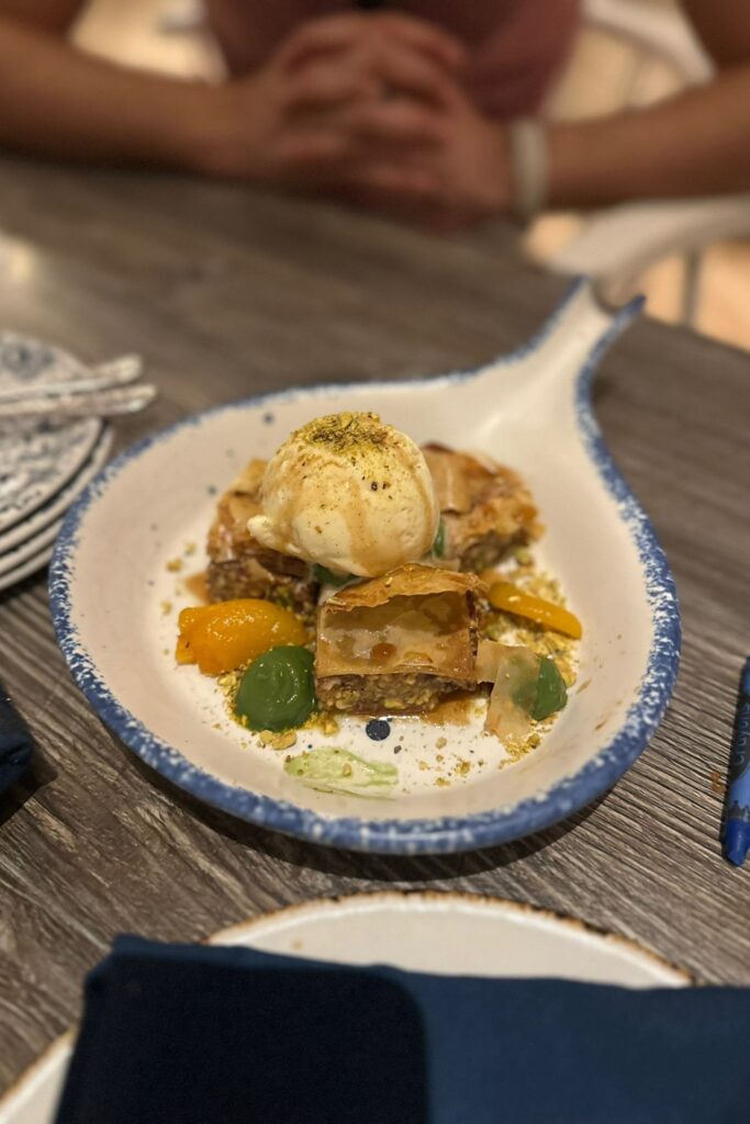 Baklava served with vanilla ice cream, pistachio crumble, and candied citrus on a blue-rimmed ceramic plate at a Baha Mar restaurant.