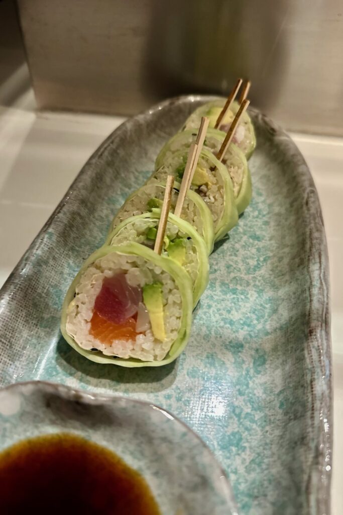 Cucumber-wrapped sushi roll with tuna, salmon, and avocado served on a blue ceramic plate with soy sauce at Katsuya, Grand Hyatt Baha Mar.
