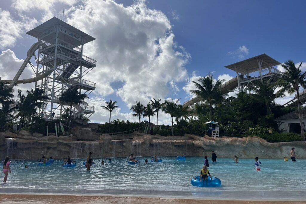 The wave pool and tall water slide towers at Baha Bay water park at Grand Hyatt Baha Mar, with guests floating on blue tubes in Nassau, Bahamas.